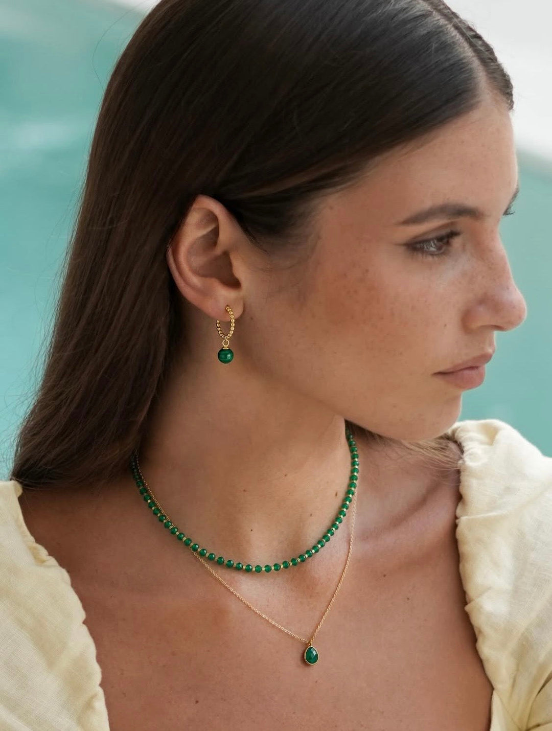 Woman wearing layered green gemstone necklaces and gold hoop earrings with green pendant details.