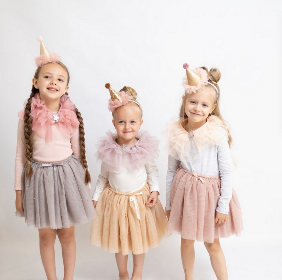 Three girls wearing Billy Loves Audrey party accessories, including tulle skirts, ruffle collars, and glitter party hats.