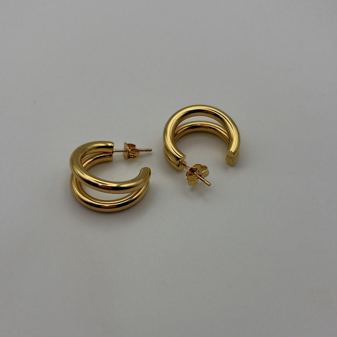 Polished gold double hoop earrings with a modern layered design on a white background