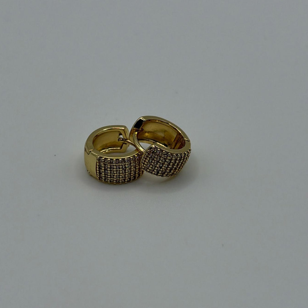 Gold pavé huggie earrings with sparkling crystal detailing and polished finish on a white background