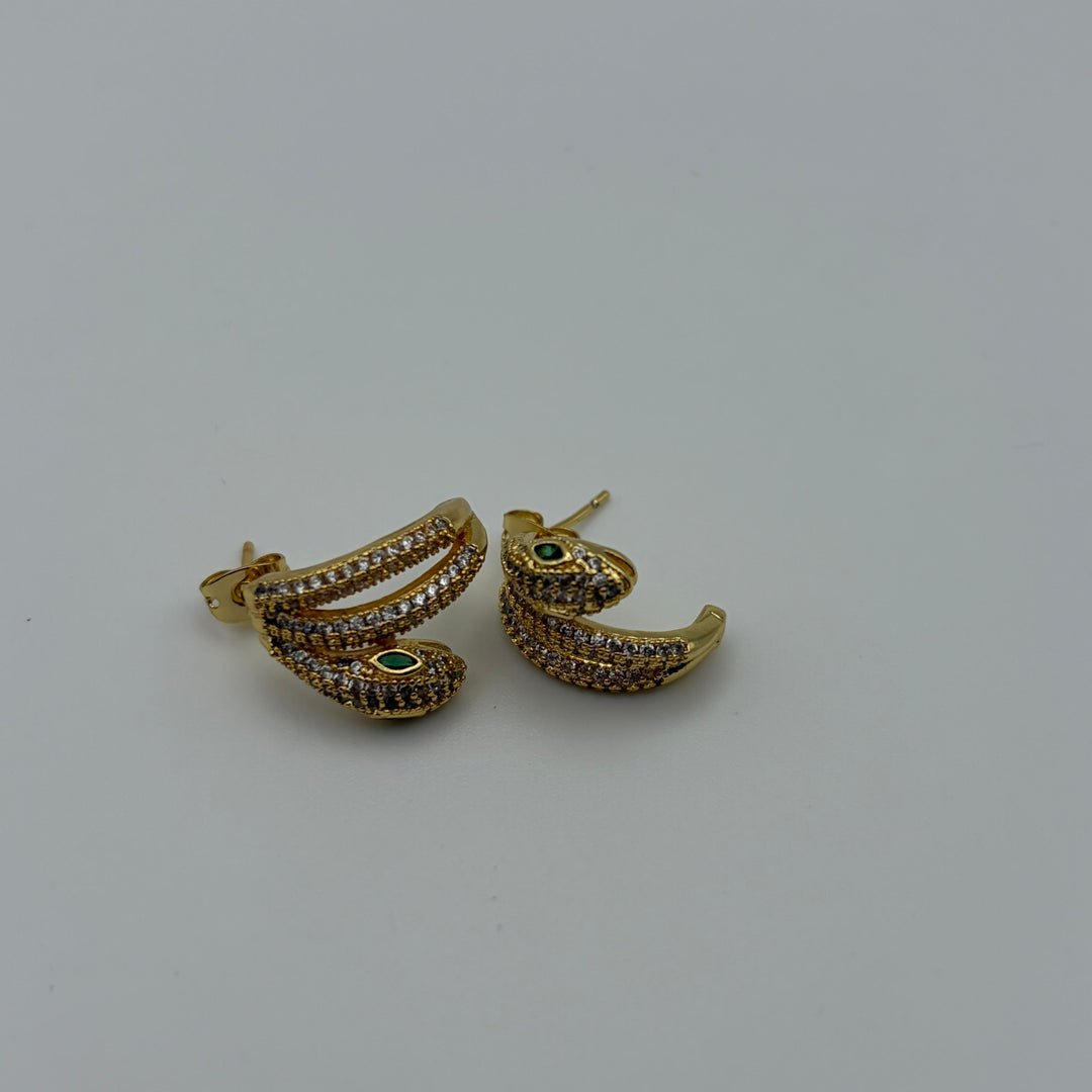 Gold snake earrings with pavé crystals and emerald green eyes on a white background